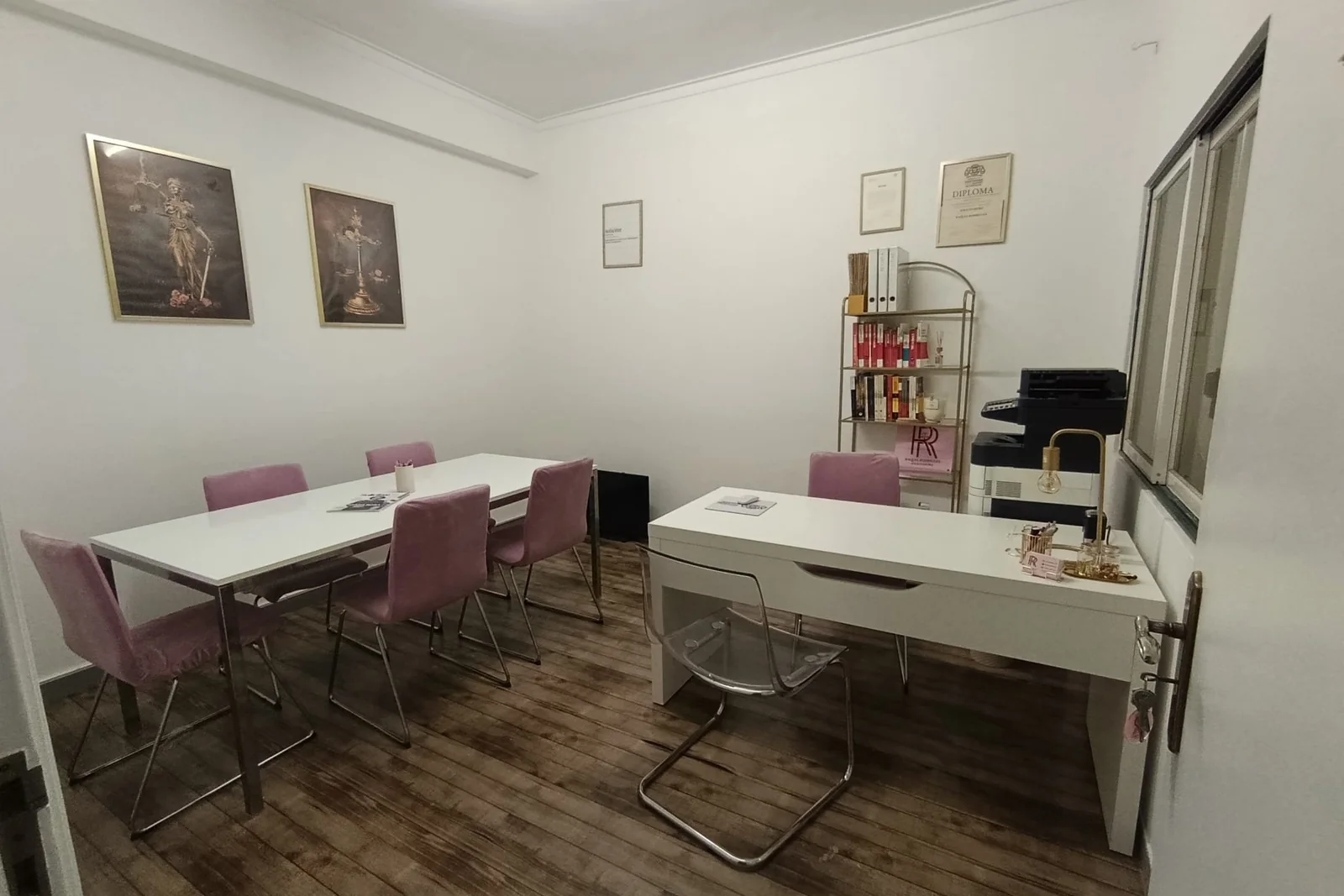Sala de atendimento do escritório, com mesa de reuniões e cadeiras cor-de-rosa